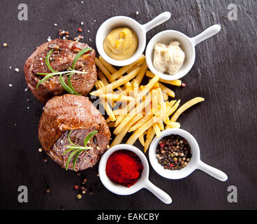 Morceaux de viande rouge avec des steaks frites et des épices, servi sur la surface de la pierre noire. Banque D'Images