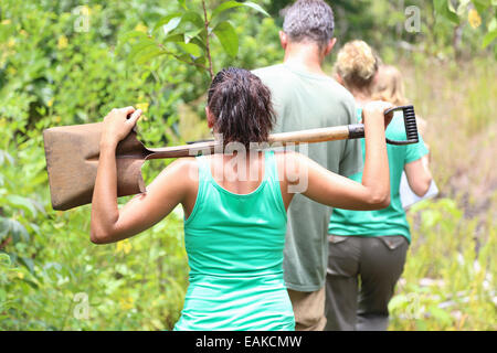 Vue arrière du woman wearing green tank top transportant sur les épaules à travers jardin pelle Banque D'Images