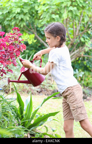 Girl watering plants in garden avec arrosoir rouge Banque D'Images