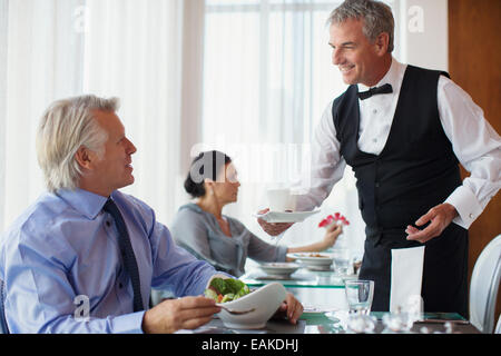 Waiter serving tasse de café à man sitting at table in restaurant Banque D'Images