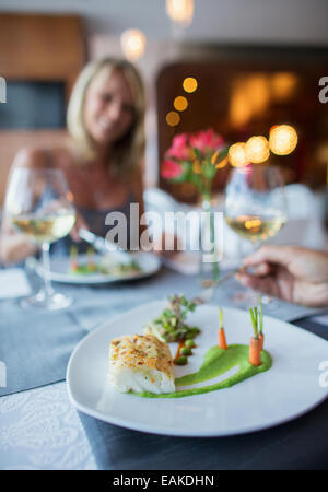 Close up of plaqués platine avec poisson et carottes sur restaurant table, woman in background Banque D'Images