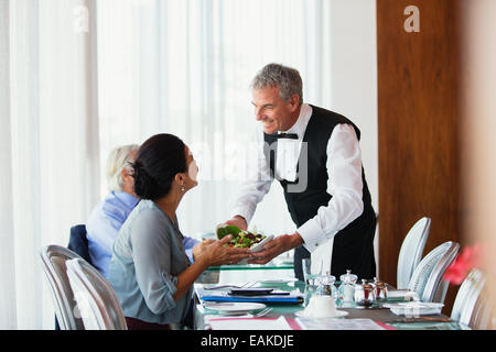 Smiling waiter serving salad to woman sitting at table in restaurant Banque D'Images