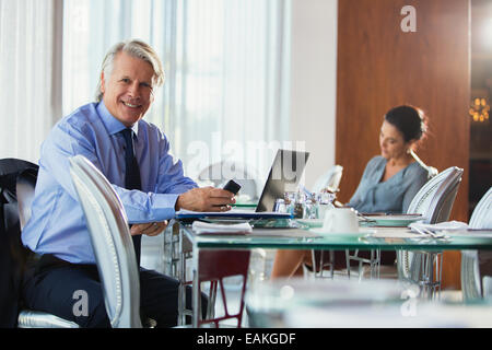 Portrait of smiling businesswoman with smart phone and laptop in restaurant Banque D'Images