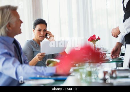 Businesswoman looking at chart et talking on mobile phone at restaurant table Banque D'Images