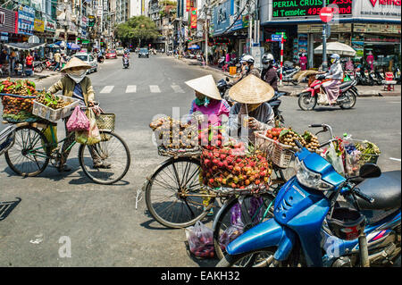 Les fournisseurs traditionnels des femmes à chapeaux coniques vendent des fruits en provenance de leurs bicyclettes dans la rue près du marché Ben Thanh, Ho Chi Minh Ville. Banque D'Images