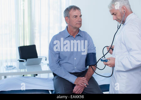 Mature doctor en tenant la pression artérielle du patient in office Banque D'Images