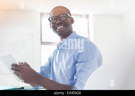 Portrait of young businessman wearing glasses and blue shirt holding digital tablet in office Banque D'Images