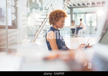 Woman using digital tablet in office, des collègues en arrière-plan Banque D'Images