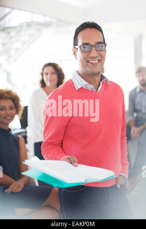 Portrait of smiling businessman wearing glasses et rose sweatshirt holding documents, l'équipe du bureau en arrière-plan Banque D'Images