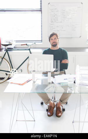 Portrait de l'homme assis avec les bras croisés derrière le verre 24 dans un bureau moderne, location et de tableau blanc en arrière-plan Banque D'Images