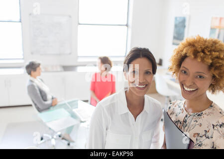 Portrait of two smiling business women in office, colleagues talking in background Banque D'Images