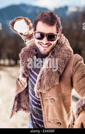 Un jeune homme portant un manteau en peau de jouer avec une boule de neige Banque D'Images