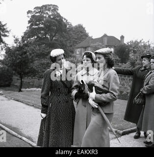 Années 1950, image historique montrant trois jolies jeunes femmes debout ensemble à l'extérieur, élégamment habillées à la mode du jour, avec des chapeaux, manteaux et sacs à main, Angleterre, Royaume-Uni. Banque D'Images