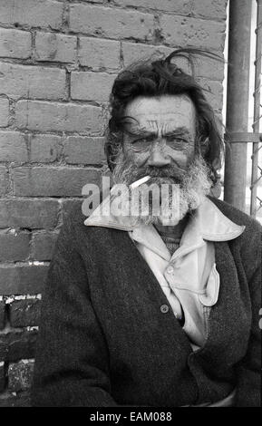 Années 1970, portrait d'un homme adulte déchu, avec des cheveux sauvages et une barbe méconnue et avec une cigarette dans la bouche, une personne qui a eu des moments difficiles, sans-abri, une personne de la rue, Los Angeles, Californie, ÉTATS-UNIS. Certaines parties de LOS ANGELES sont connues sous le nom de « ville en carton » où un grand nombre de sans-abri désespérés vivent une existence du main à la bouche dans la rue. Banque D'Images