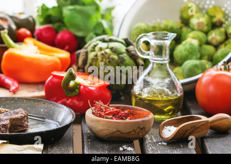 Variation de légumes frais, les tomates, le poivre, le paprika, l'artichaut et les choux de Bruxelles sur l'ancienne table près de fenêtre dans la lumière du jour. Banque D'Images