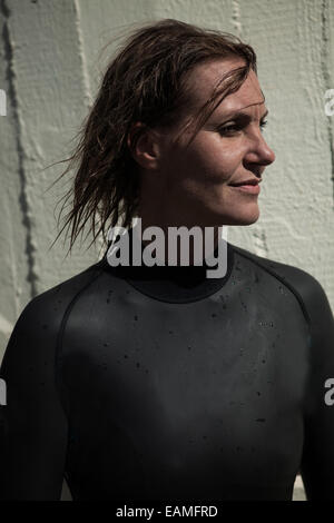 Nageuse attractive brunette wearing wetsuit noir avec les cheveux mouillés et à la calmement avec léger sourire et de la lumière du soleil en face Banque D'Images