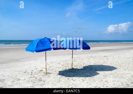 Parasol : deux parasols de plage sont placés sur la plage en face d'un beau ciel bleu avec des nuages. Banque D'Images