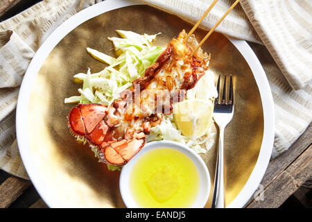 Brochettes de queue de homard principal dans le shell frit avec flash et beurre Citron Citrons et laitue sur une plaque d'or Banque D'Images