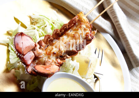 Brochettes de queue de homard principal dans le shell frit avec flash et beurre Citron Citrons et laitue sur une plaque d'or Banque D'Images