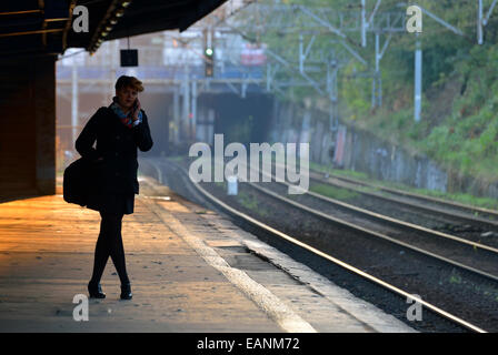 Woman talking on mobile phone sur la plate-forme de la gare Warszawa Ochota au lever du soleil, Varsovie, Pologne Banque D'Images