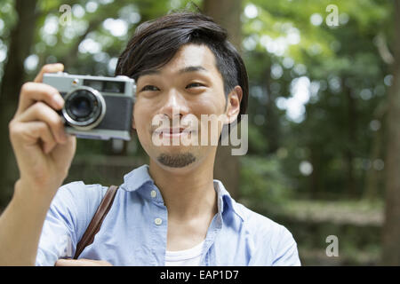 Un homme dans un parc de Kyoto tenant un appareil photo, prendre une photo. Banque D'Images
