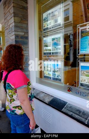 Une jeune femme adulte à la recherche dans la fenêtre d'un agent immobilier.Padstow Cornwall England UK Banque D'Images