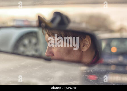 Visage de femme dans la voiture rétroviseur intérieur lors de la conduite à travers la ville aux heures de pointe de trafic Banque D'Images