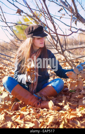 Fille avec regard pensif assis près d'un arbre avec des feuilles sèches dans la main Banque D'Images