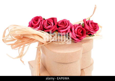 Quelques cadeaux en forme de cœur attaché avec du raphia naturel et artificiel garni de roses rouges sur fond blanc Banque D'Images