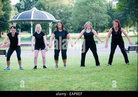 Cinq femmes en surpoids dans sport clothese s'amusant à un camp d'entraînement dans un parc tôt le matin dans l'été de faire des squats Banque D'Images