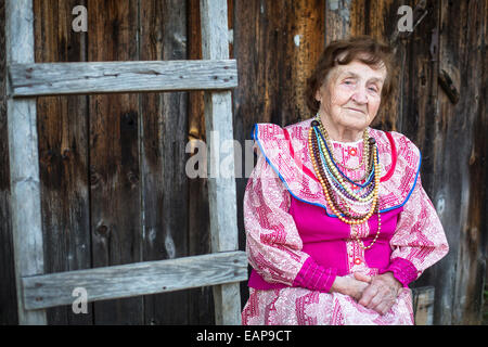 Vieille Femme en rouge et blanc ethnique robe et collier, à l'extérieur dans le village. Banque D'Images