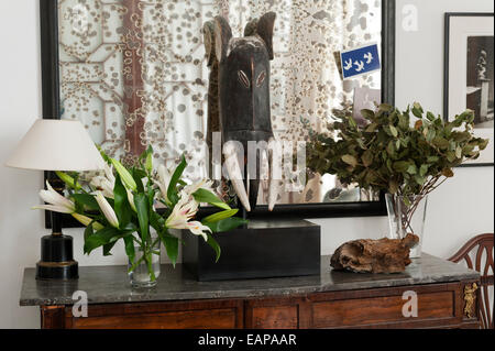 La sculpture africaine sur console recouvert de marbre table avec verre de nénuphars et lampe. Un miroir antique qui est dans l'arrière-plan Banque D'Images