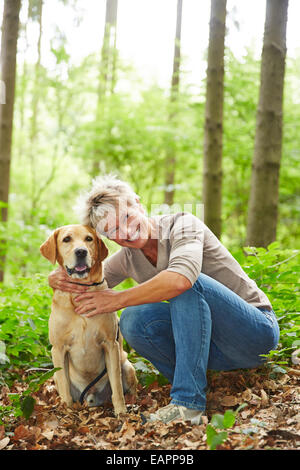 Smiling senior woman sitting with labrador retriever dog in a forest Banque D'Images