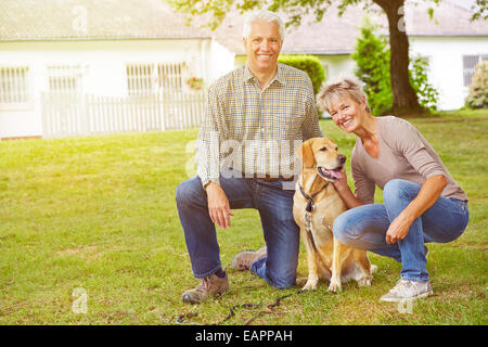 Happy senior couple sitting avec maison et-labrador retriever dans un jardin Banque D'Images