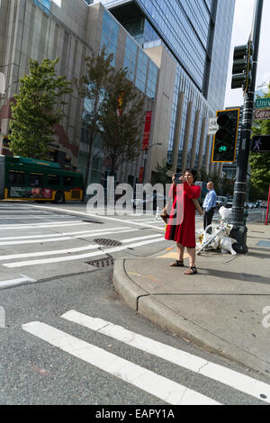 Femme dans un manteau rouge de prendre une photo avec son smartphone, tablette, grand en étant debout sur un trottoir Banque D'Images
