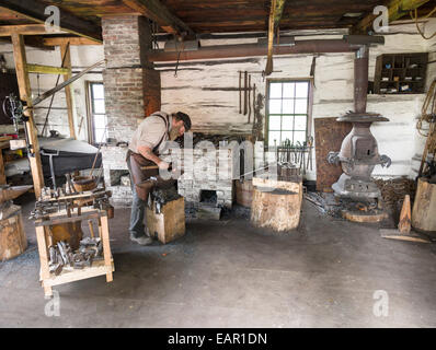 Marteau de forgeron. Un forgeron marteaux un morceau de fer sur une enclume, entouré par son atelier. Banque D'Images