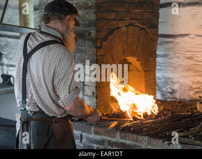 Forgeron au sa forge. Un forgeron chauffe le fer à repasser avec sa main droite tout en pompant le soufflet avec sa gauche. Fire et pousse Banque D'Images