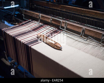 Volant sur un tissu à rayures. Un volant avec la laine blanche repose sur un morceau de tissu à rayures étant tissés sur une usine vintage Banque D'Images