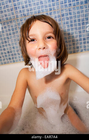 Six ans dans un bain de mousse poussant sa langue dehors. Banque D'Images