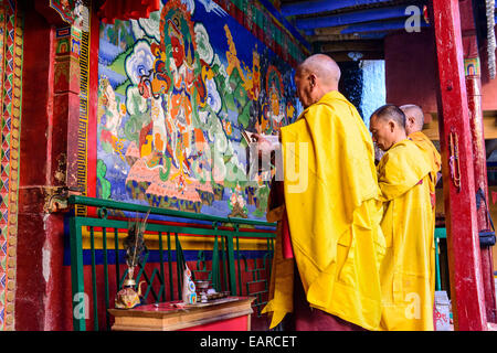 Trois moines de Lamayuru Gompa priant devant une peinture murale religieuse colorés, le Ladakh, le Jammu-et-Cachemire, l'Inde Banque D'Images