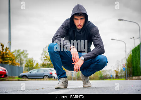 Beau jeune homme avec capuche et chapeau de base-ball en ville rue, looking at camera Banque D'Images