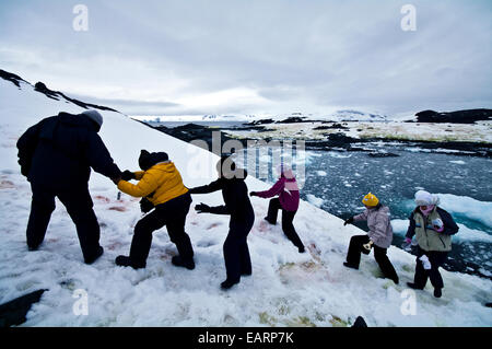 Les touristes s'entraider pour escalader une pente enneigée en Antarctique. Banque D'Images