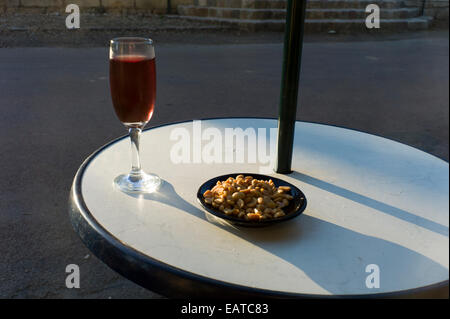 Verre de vin rose et arachides sur cafe table, soleil du soir Banque D'Images