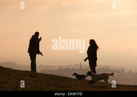 Jeune couple à prendre des photos sur le téléphone comme le coucher de soleil sur camp britannique sur les collines de Malvern, Herefordshire, Angleterre, RU Banque D'Images