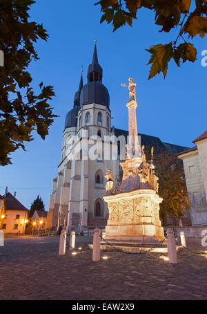 Trnava - l'église gothique Saint Nicholas au crépuscule et st. Joseph colonne baroque. Banque D'Images