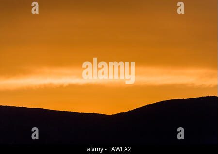 Un coucher du soleil orange luminescent sur une silhouette d'une ligne de crête de montagne. Banque D'Images