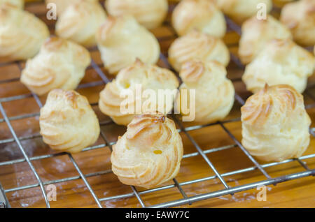 Choux frais crème sur une grille de refroidissement sur table en bois Banque D'Images