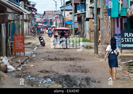 Une écolière promenades le long d'une rue de terre dans le district de port d'Iquitos. Banque D'Images