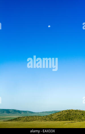 Lever dans un ciel bleu clair sur une savane luxuriante plaine et collines basses. Banque D'Images