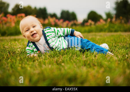 Cute baby looking at camera et souriant tout en étant allongé sur l'herbe en plein soleil Banque D'Images